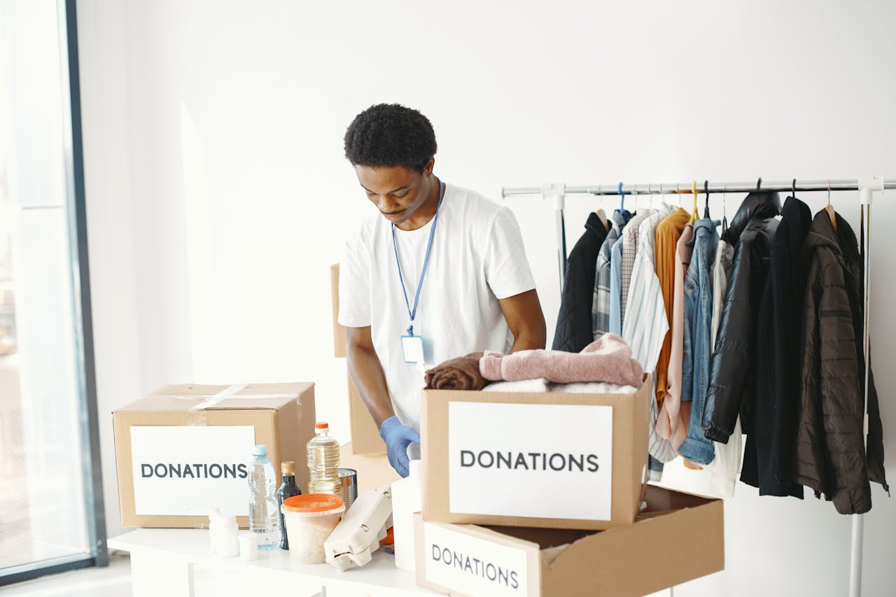 A volunteer organizes donations in a community center, featuring boxes labeled "Donations" and a clothing rack.